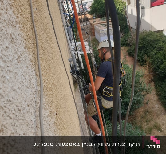 עובד בגובה עם קסדה ורתמה על קיר בניין